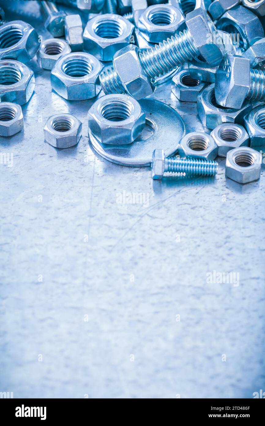 Pile of stainless steel threaded screws nuts and bolts washers on metallic background
