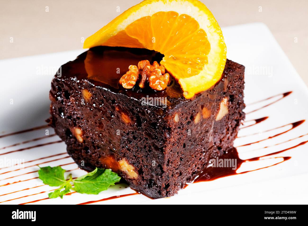 Fresh baked delicious chocolate and walnuts cake with slice of orance on top and mint leaf, food photography Stock Photo
