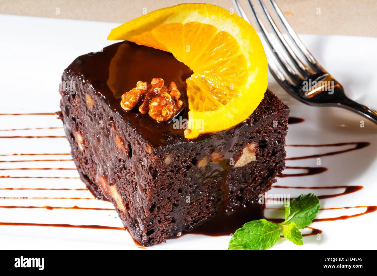 Fresh baked delicious chocolate and walnuts cake with slice of orance on top and mint leaf, food photography Stock Photo