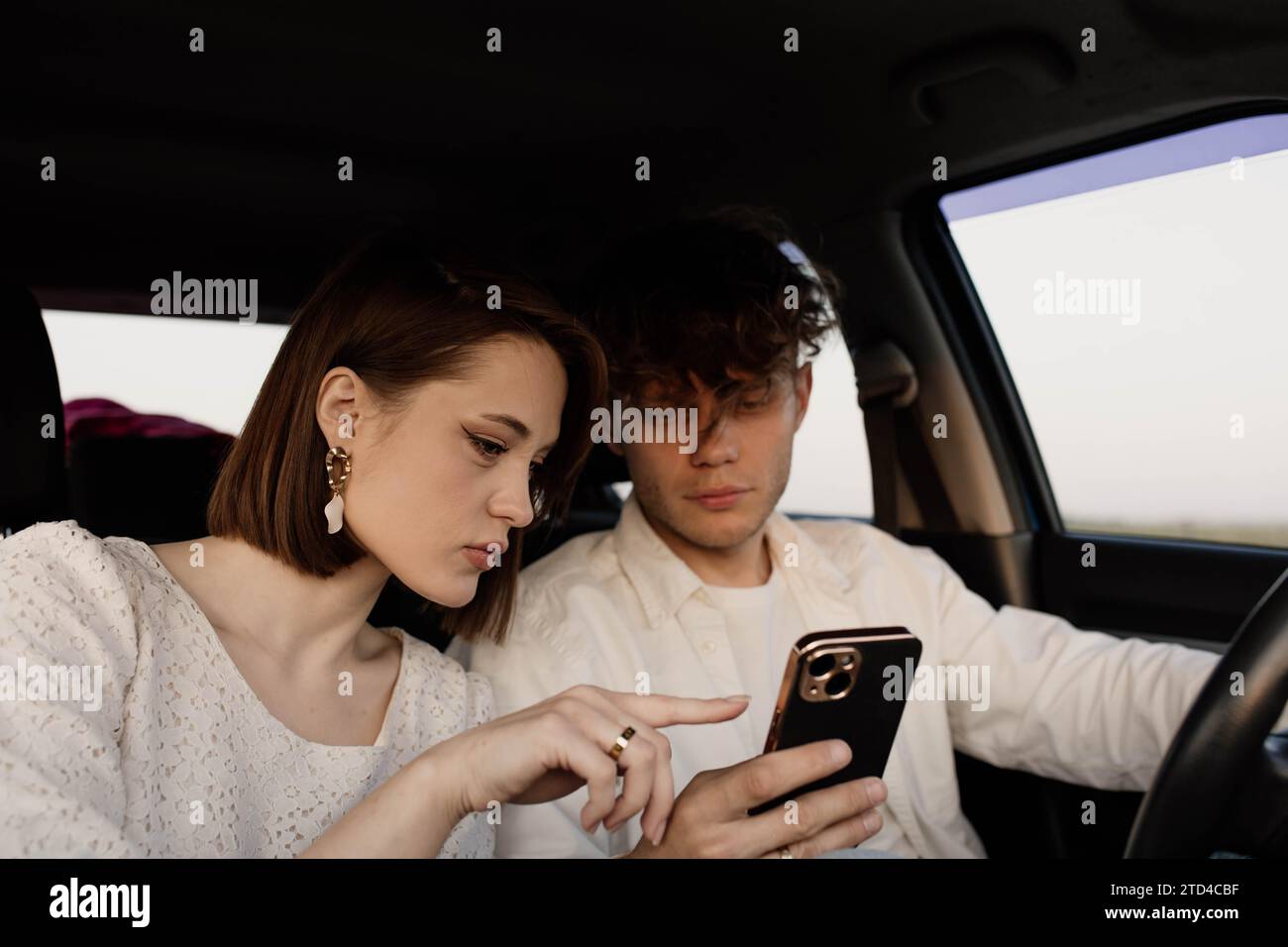 Beautiful young couple in love in a car looking at a weekend travel route on a smartphone Stock Photo