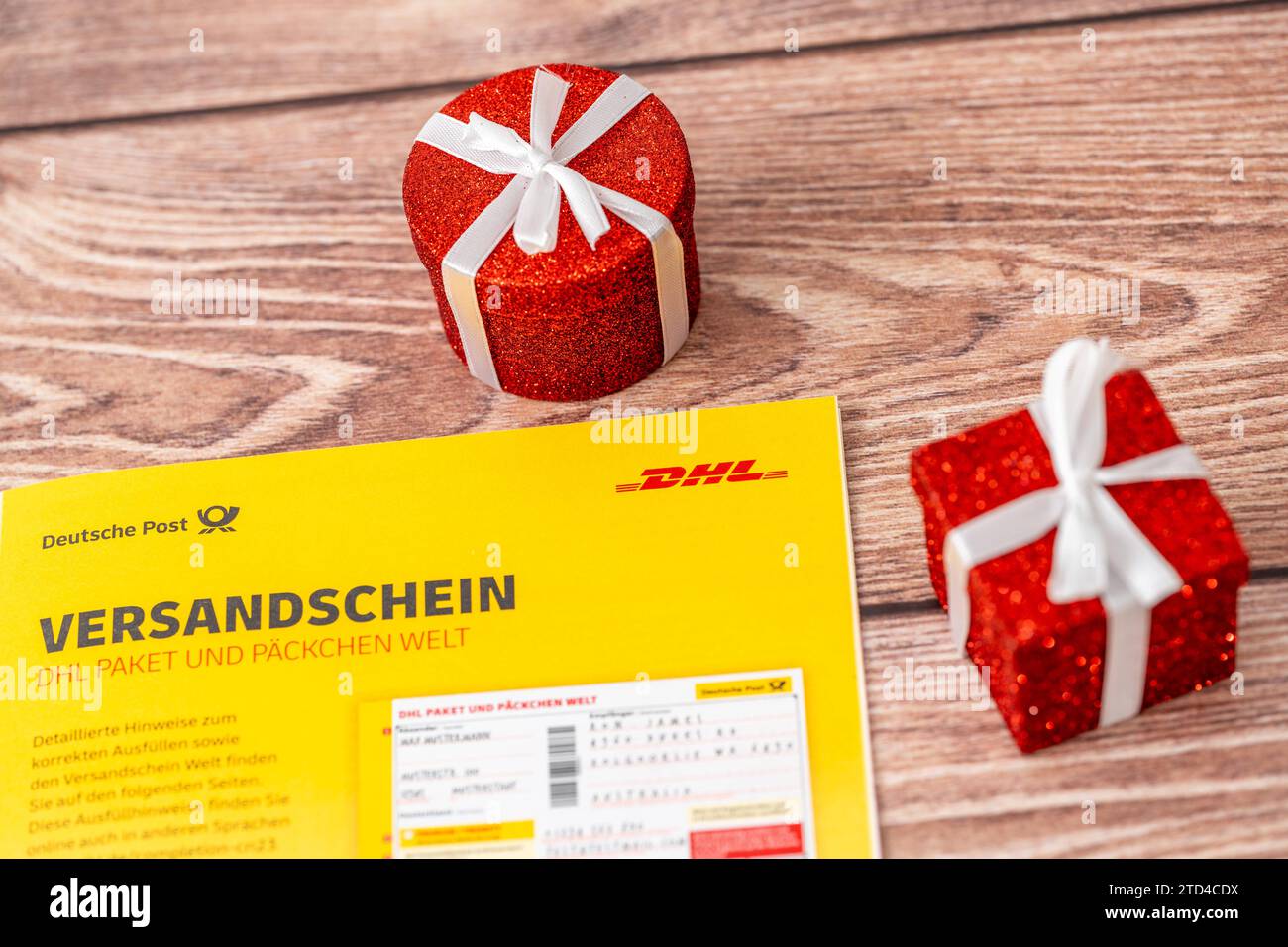Augsburg, Bavaria, Germany - December 15, 2023: DHL parcel and parcel shipping label next to decoration for Christmas, a red wrapped gift *** DHL Paket und Päckchen Versandschein neben Dekoration zu Weihnachten, einem roten verpackten Geschenk Stock Photo
