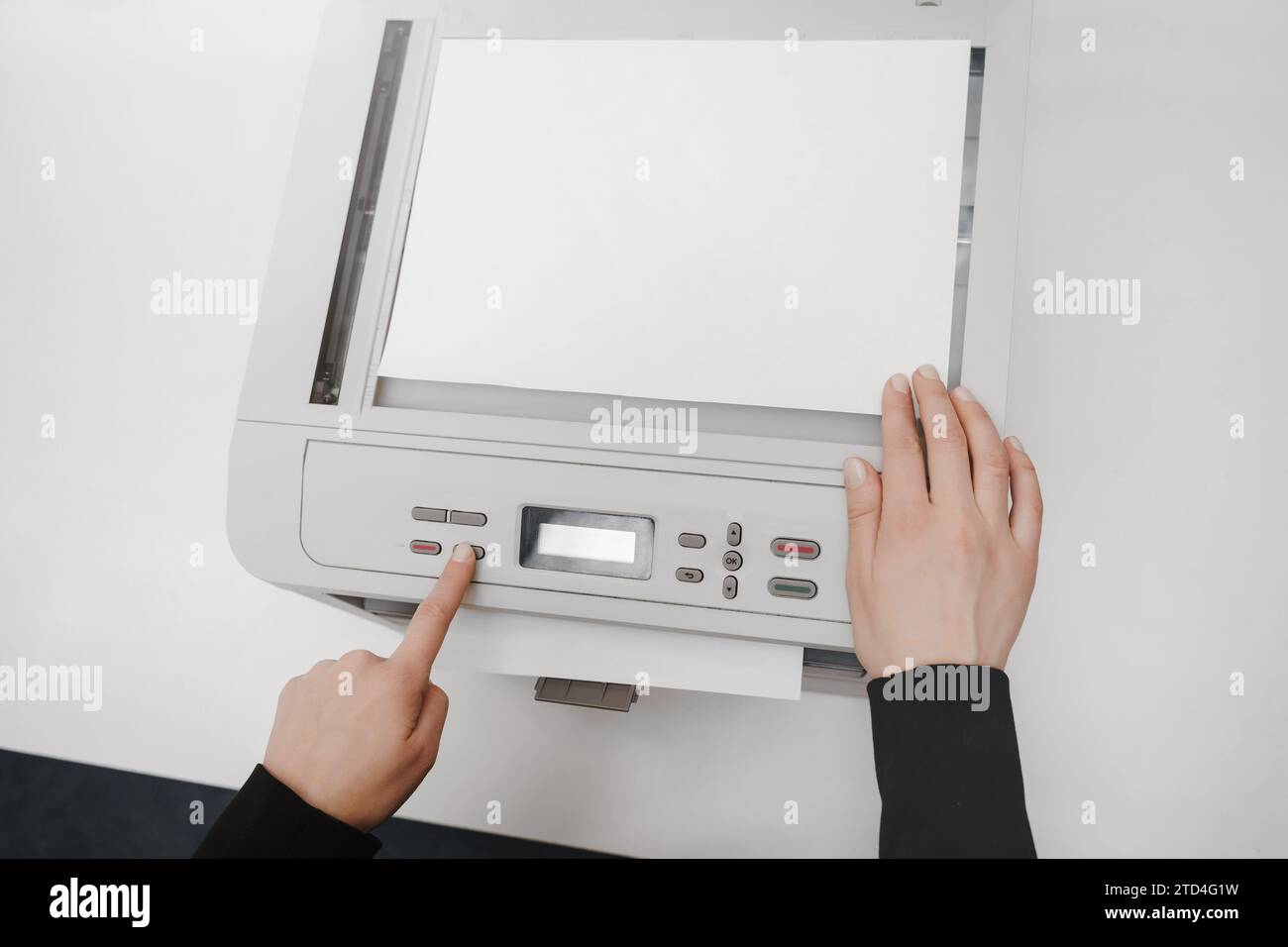 The hands of a young woman is placing a piece of paper on a flatbed ...