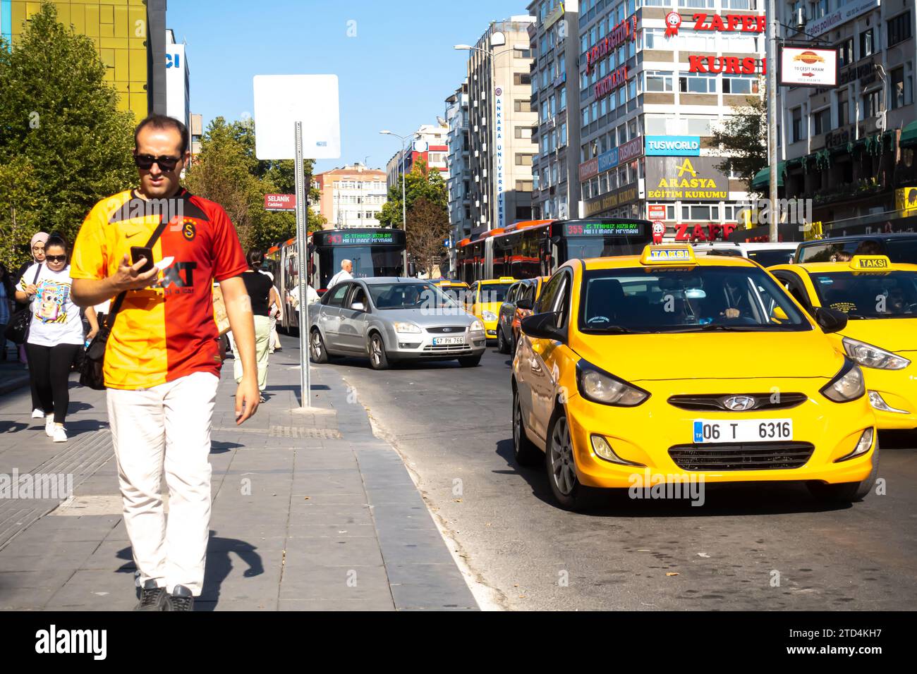 Turkish man is walking while looking at his smart phone, yellow taxi cabs passing by in Ankara Turkey Stock Photo