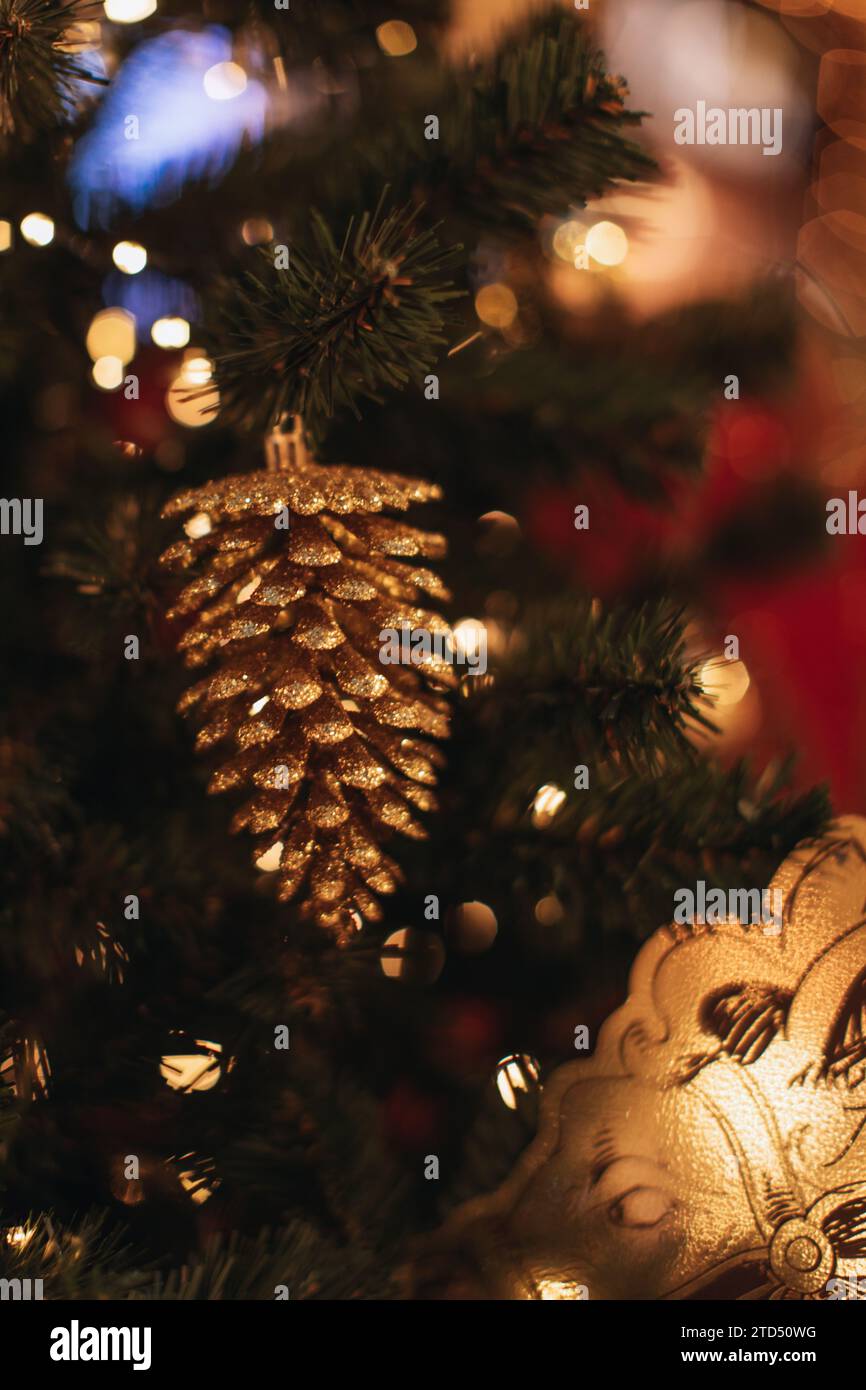 Golden glossy pine cone hanging on a Christmas tree with flashing golden lights. Decorated spruce branches Stock Photo