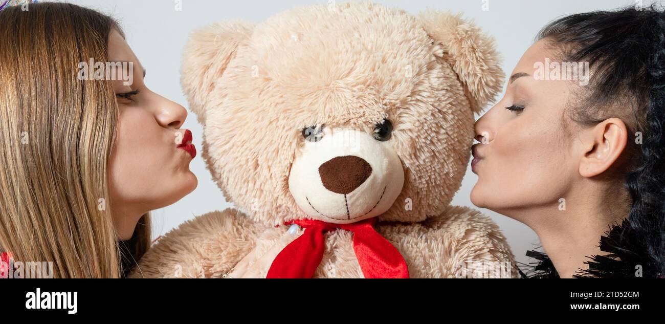 Two young women celebrate New Year with shiny props, kissing teddy bear Stock Photo