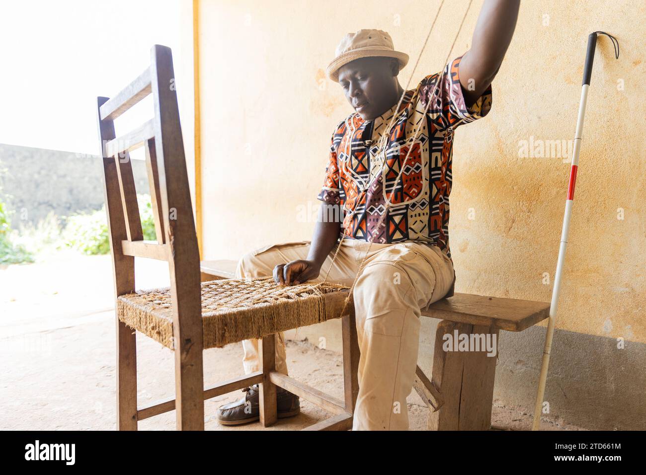 Blind African man sitting, engaged in weaving a dining chair. Blindness and work concept. Stock Photo