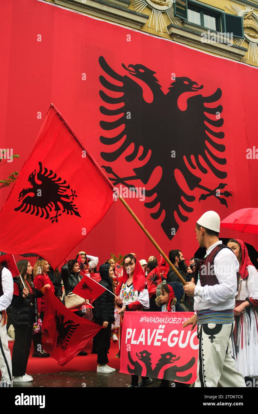 Tirana, Albania - November 28, 2023: On a rainy Independence Day, Tirana City Hall is covered with a massive Albanian flag. Citizens pass by the flag- Stock Photo
