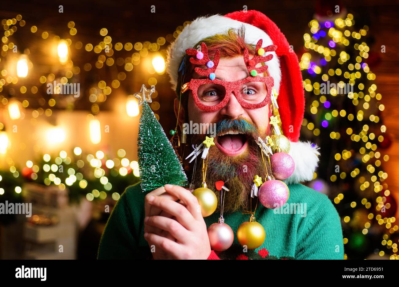 Happy bearded man in Santa hat and party glasses with small Christmas tree. Santa man with Christmas beard style. Santa with Christmas decoration Stock Photo