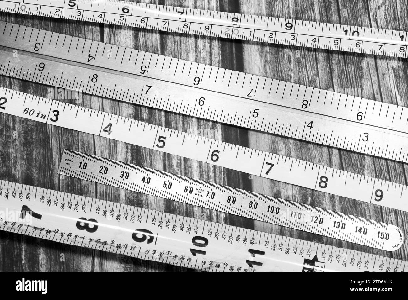 Black and white image of a variety of tape measures on wooden bench Stock Photo