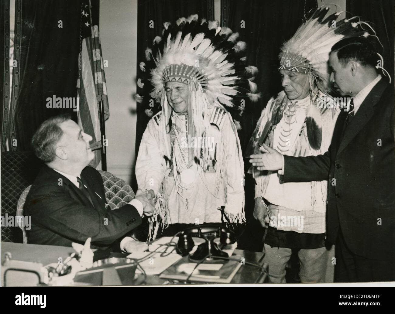 Washington DC, 01/13/1938. Indians visit the great white father. President of the United States of America Franklin D. Roosevelt, seated, greets Drags Wolf, left, and Folish Bear, right, while Arthur Mandan, chief of the tribal council, interprets for the Indians. The reason for the visit was to thank the great white father for his help in restoring the 'Sacred Bundle' against drought, of the Watherbuster clan of the Gros ventres tribe of North Dakota. A tribal relic whose loss in 1907 was related to a great period of drought like none of them remembered. With the return of the package, the In Stock Photo