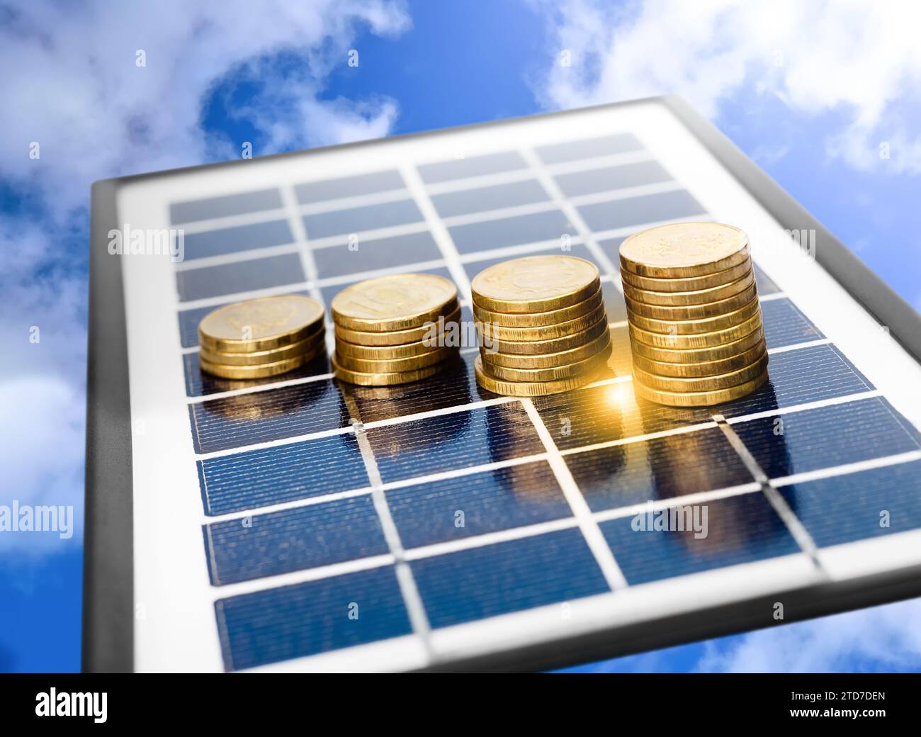 Stacks of yellow coins on a solar panel against a background of a blue sky with clouds. Concept of solar energy, saving and environmental friendliness Stock Photo