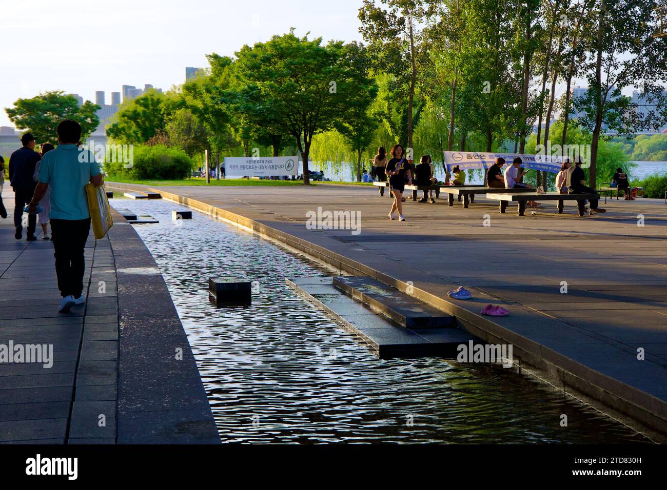 Seoul, South Korea - June 3, 2023: Visitors stroll beside the Waterlight Square Fountain's stream in Yeouido Hangang Park, surrounded by green trees n Stock Photo