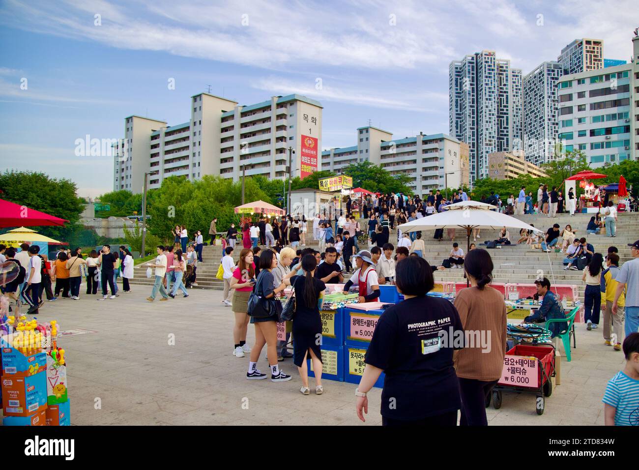 Seoul, South Korea - June 3, 2023: A bustling scene at Yeouido Hangang Park with locals gathering near food carts and concrete stairs, showcasing urba Stock Photo