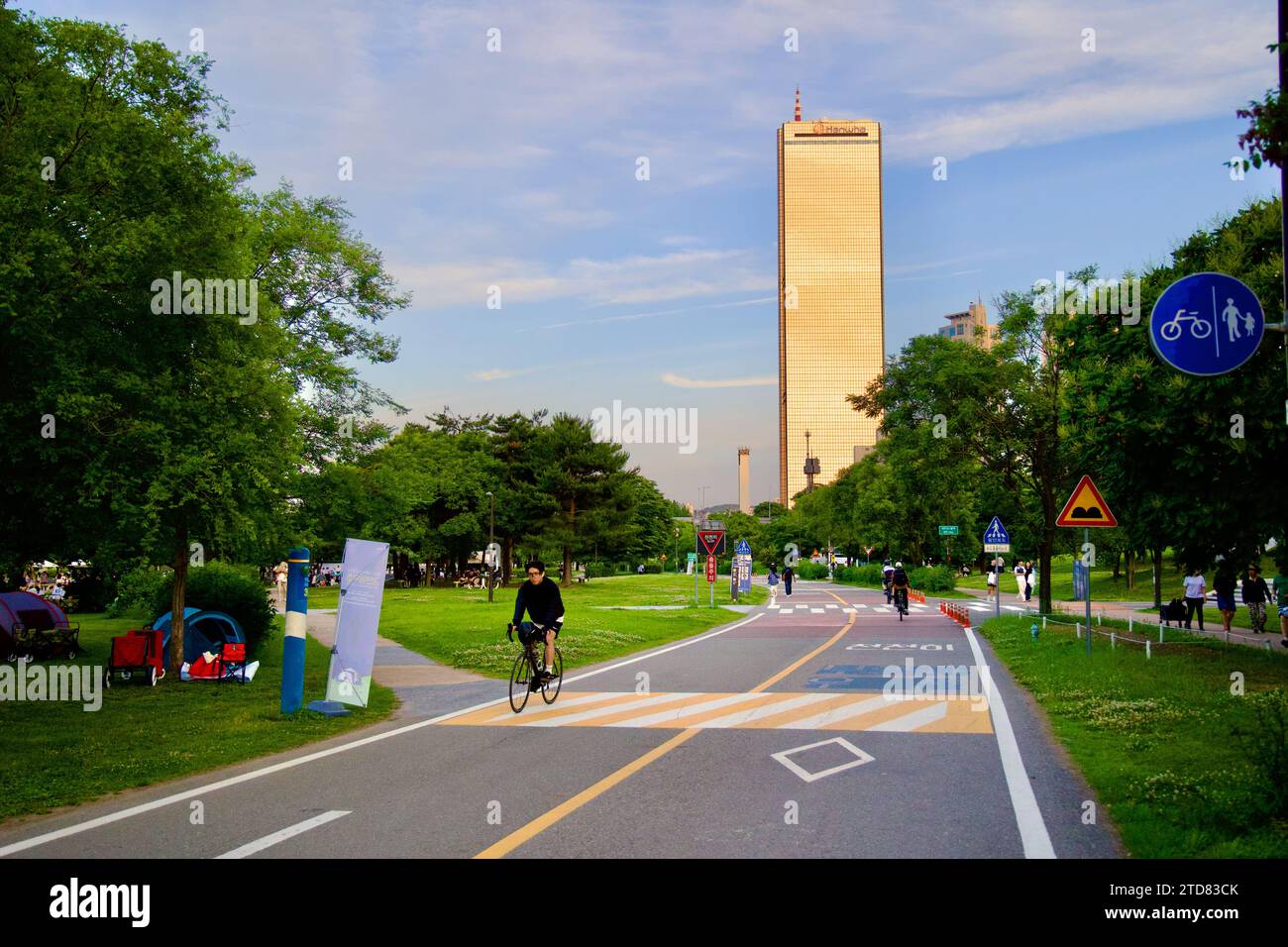 Seoul, South Korea - June 3, 2023: The iconic 63 Building with its gold-tinted windows stands tall beside the scenic bike path in Yeouido, under a cle Stock Photo