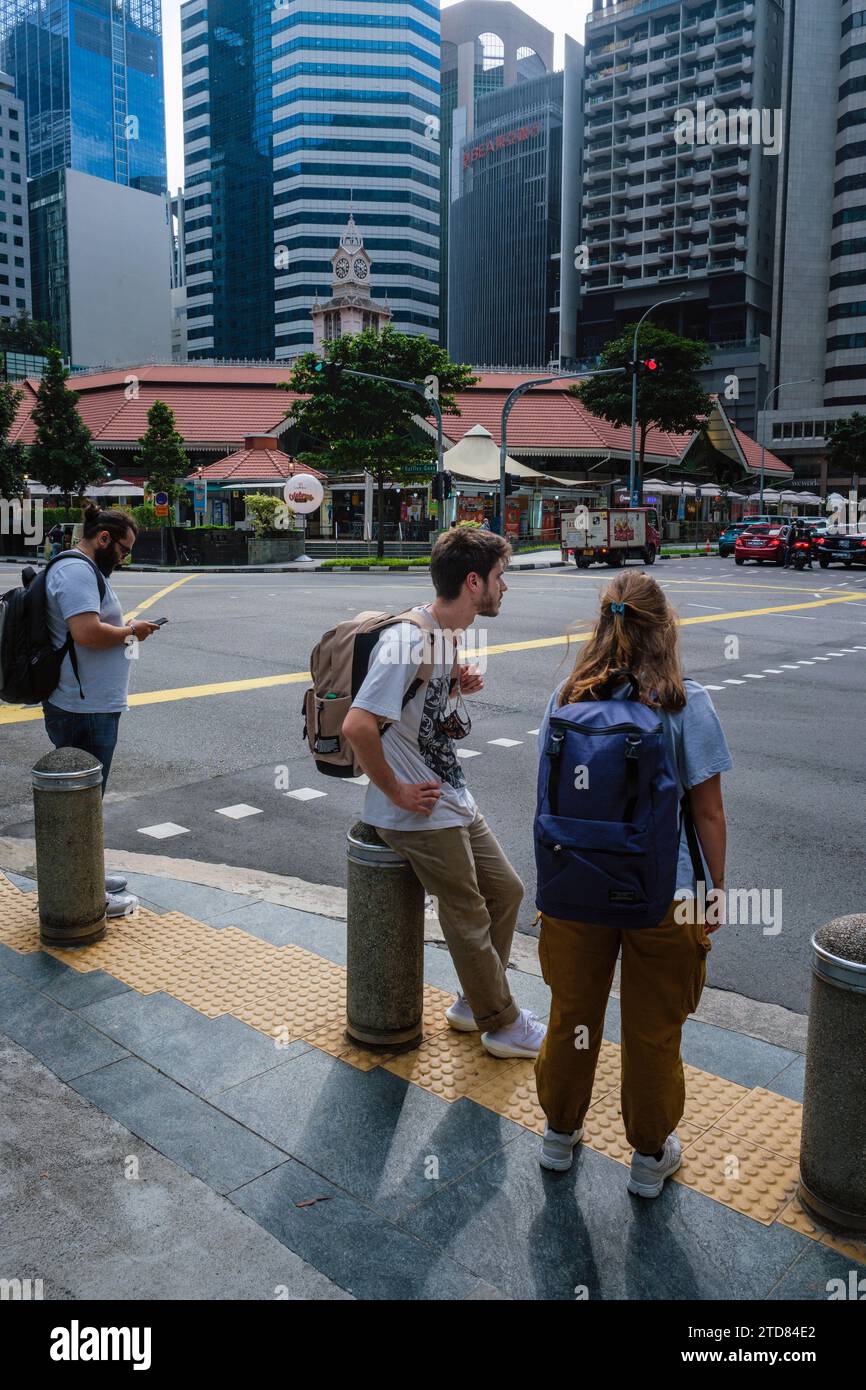 Young backpackers waiting to cross the road in Central Boulevarde by the Lau Pa Sat food market, Singapore Stock Photo
