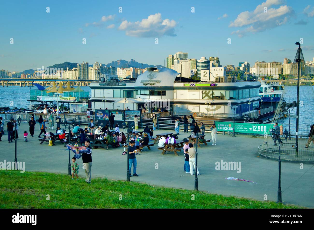 Seoul, South Korea - June 3, 2023: E-Land Cruise Ships docked at Yeouido Hangang Park, with people enjoying the riverside courtyard and picnic tables Stock Photo