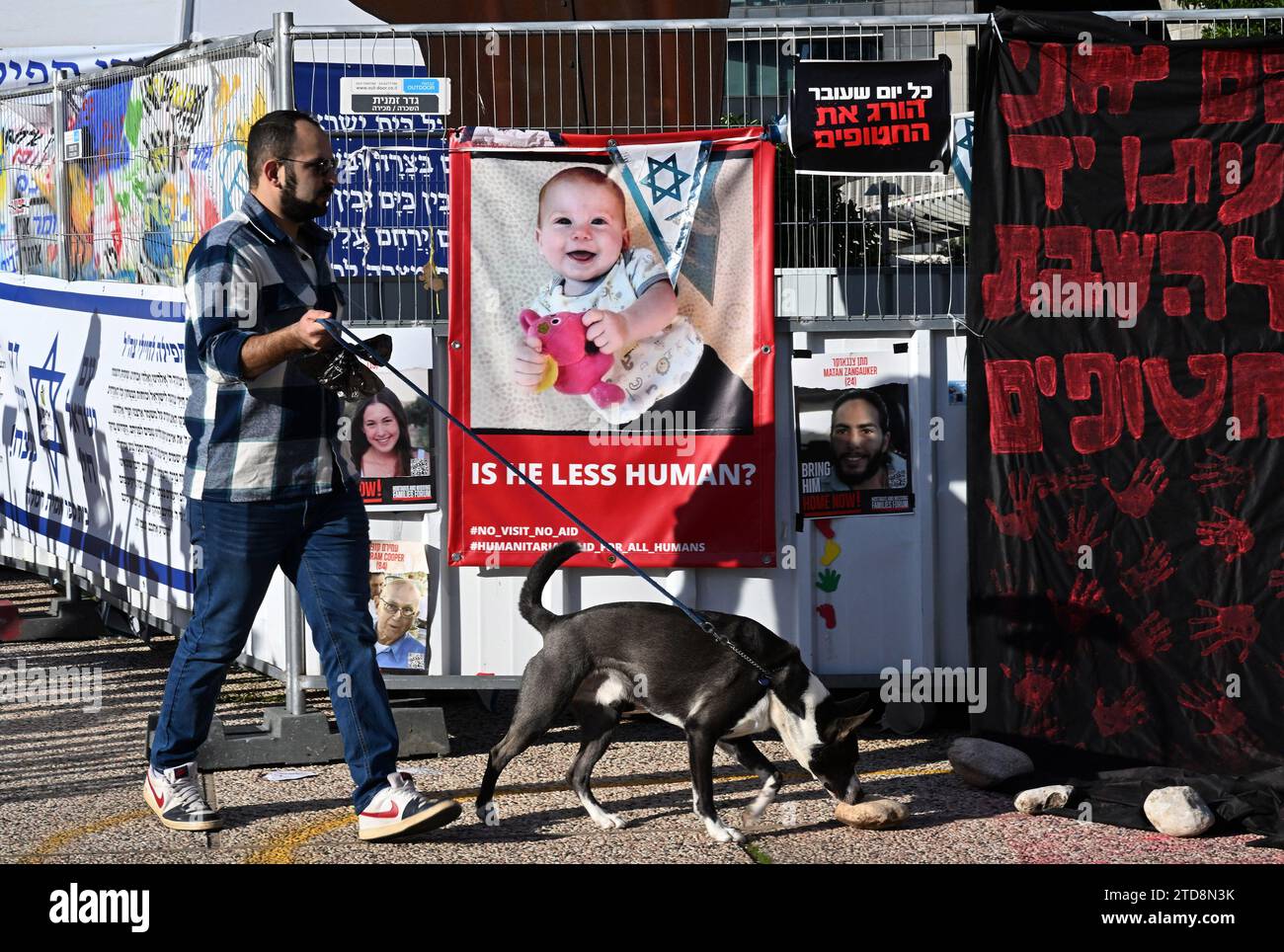 Tel Aviv, Israel. 16th Dec, 2023. A man walks a dog past a poster of a 10 month old baby Kfir Bibas held captive by Hamas in Gaza at Hostage Square outside the Tel Aviv Museum in Tel Aviv, on Saturday, December 16, 2023. Israeli forces opened fire, killing three hostages mistaken for Hamas. Photo by Debbie Hill/ Credit: UPI/Alamy Live News Stock Photo