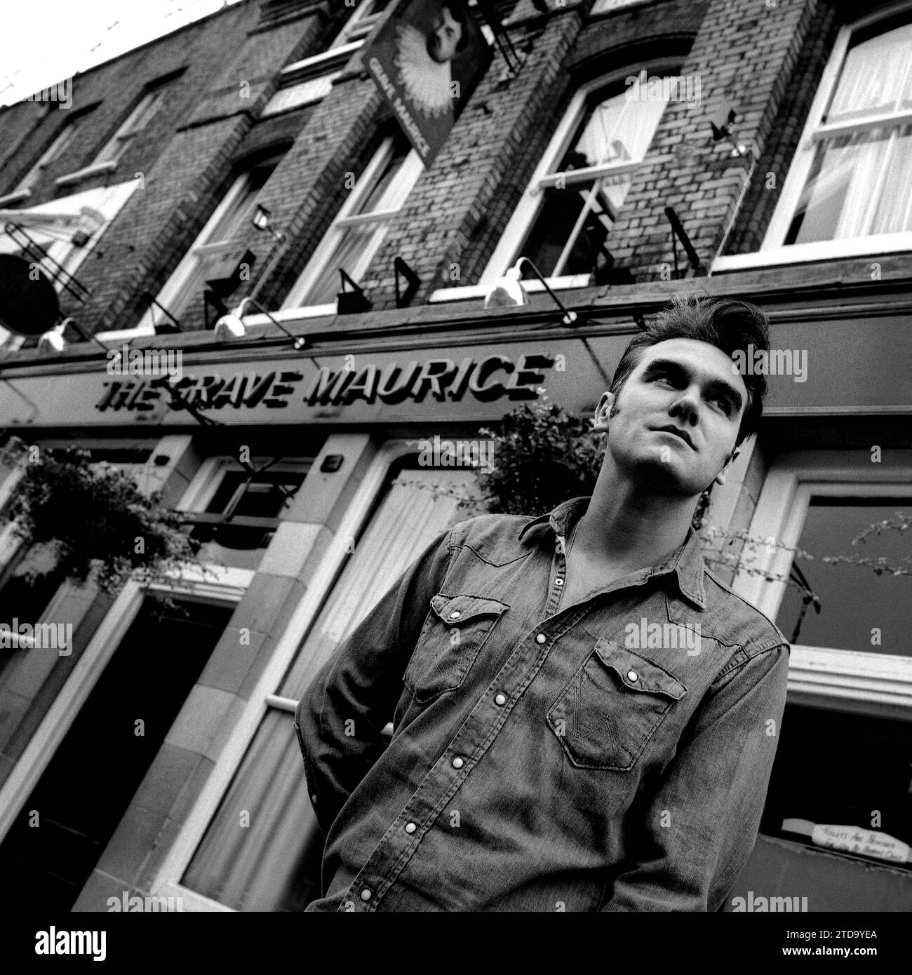 Powerful Black & white mid-shot portrait of legendary rockstar, singer/songwriter Morrissey in denim shirt. shot on the street outside The Grave Maurice pub, Whitechapel in London's East End to promote his single “Sunny” for Parlophone Records 1995. Stock Photo