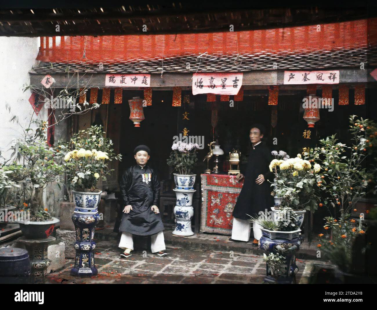Hà-nôi, Hainoi Vietnam, Tonkin, Indochina Two notables in front of the ancestral altar in the courtyard of a wealthy house, decorated with pots of chrysanthemums, at the time of the Têt festival, Festival, Clothing, Religion, Human beings, Habitat, Architecture, Inscription, information, Popular festival, Costume, New Year, Ancestor worship, Lampion, Chrysanthemum, Portrait, Altar, Vase, Dwelling, Religious or votive inscription, Furniture, Flower, Ceramics, Medal, decoration, Hairstyle, headgear, Courtyard, Smoker, Man, Indochina, Tonkin, Hanoi, Courtyard of the same house in Hanoi at the tim Stock Photo
