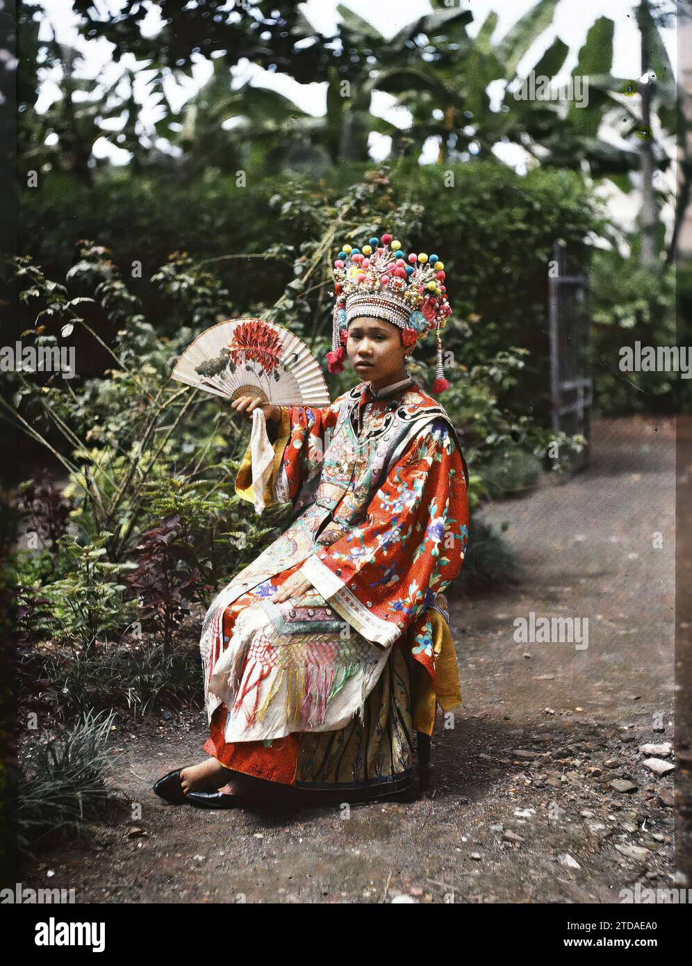 Tonkin, Indochina An actress from the Saigon Theater, in stage costume, fan spread in hand, sitting in a garden, Human beings, Clothing, Habitat, Architecture, Art, Woman, Performance costume, Shoe, Fan, Portrait, Accessory, Hairstyle, headgear, Park, Garden, Theater, Indochina, Tonkin, Actors - Saigon Theater, Solo actress, Hà-nôi, Hainoi Vietnam, 01/09/1915 - 30/11/1915, Busy, Léon, Léon Busy photographer en Indochine, Autochrome, photo, Glass, Autochrome, photo, Positive, Vertical, Size 9 x 12 cm Stock Photo
