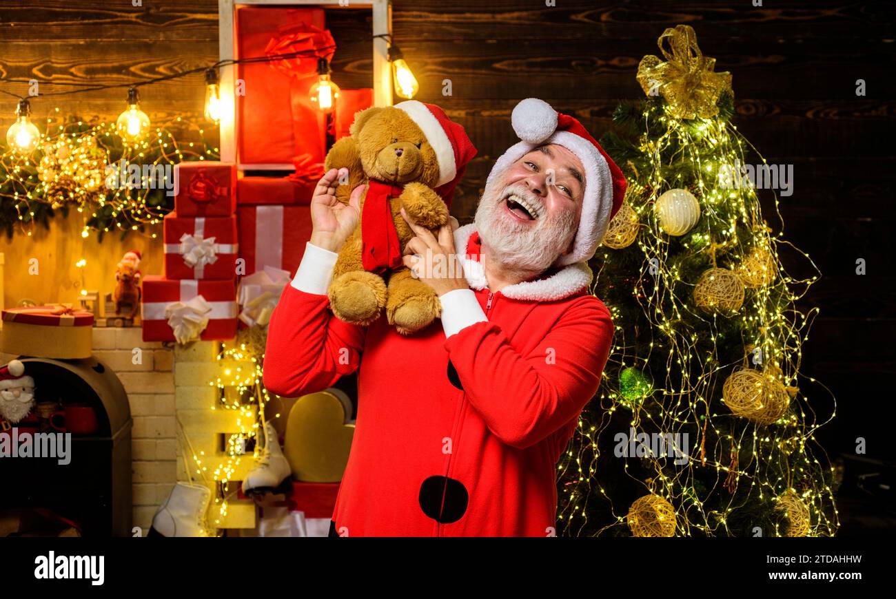 Christmas and New Year holidays. Christmas decoration. Happy Santa Claus with teddy bear on shoulder in room decorated for Christmas. Bearded man in Stock Photo