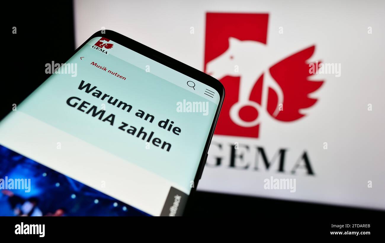 Mobile phone with website of German collecting society GEMA in front of logo. Focus on top-left of phone display. Stock Photo