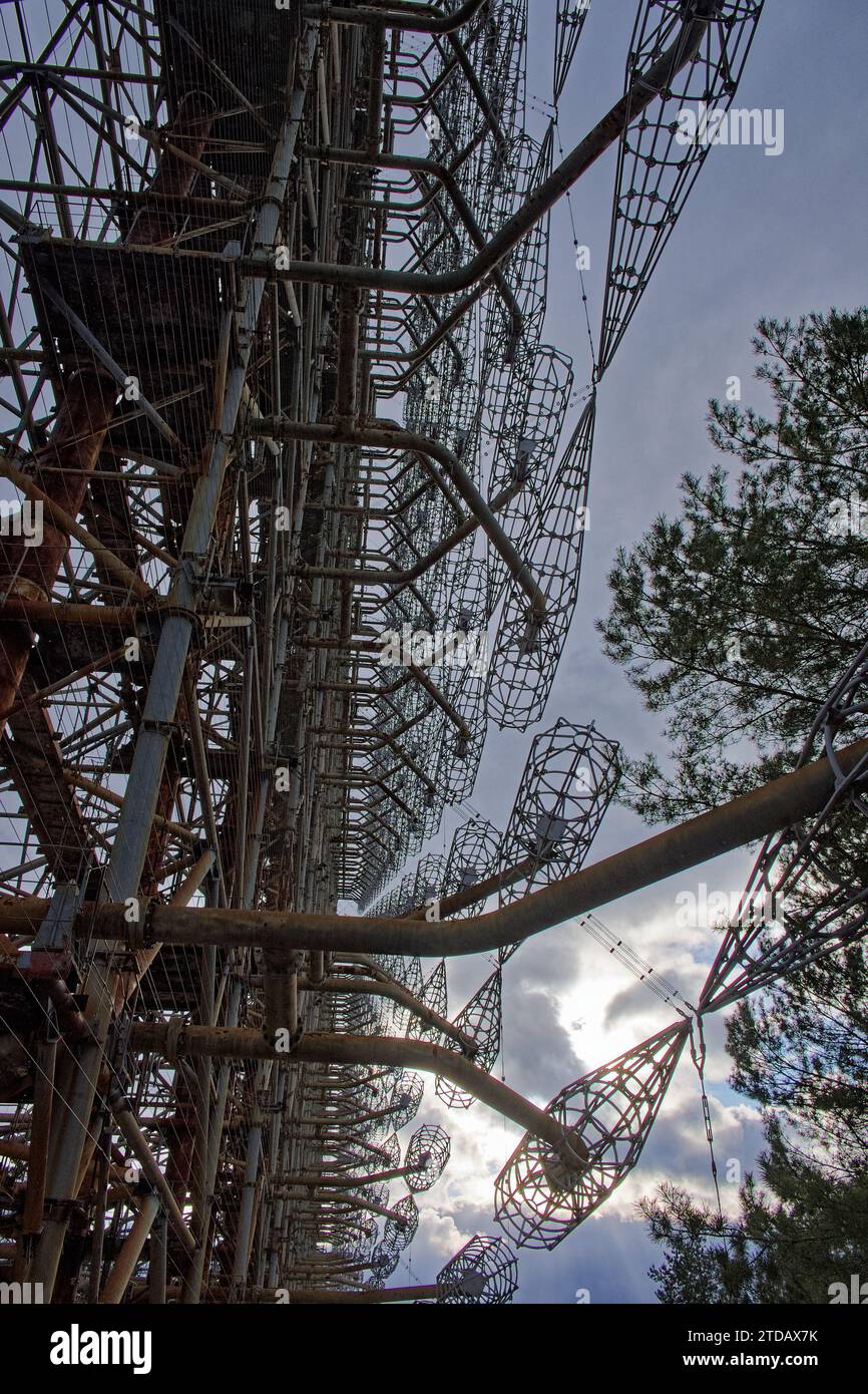 A complex structure of rusted metal beams and wire grids against a cloudy sky, surrounded by trees. Duga is a Soviet over-the-horizon radar station fo Stock Photo