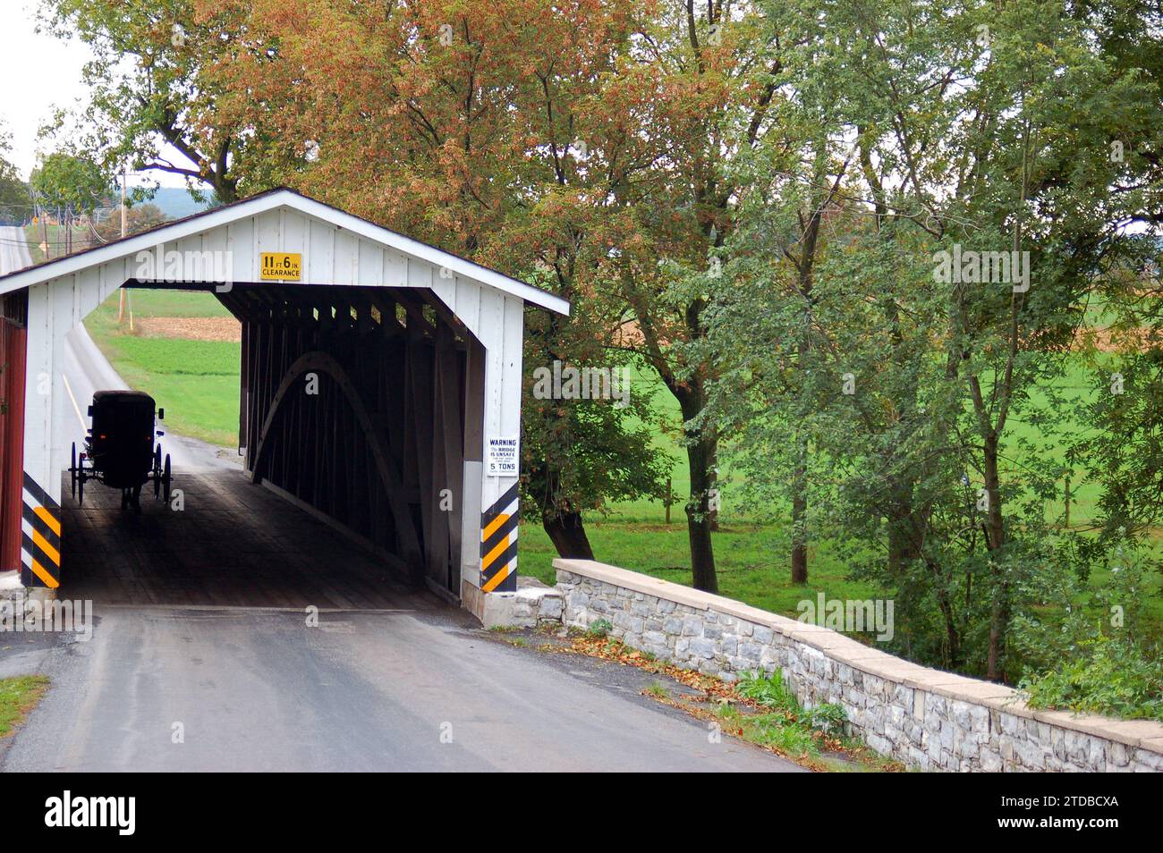 An Amish horse and buggy traverse through a covered bridge in Lancaster County, Pennsylvania Stock Photo