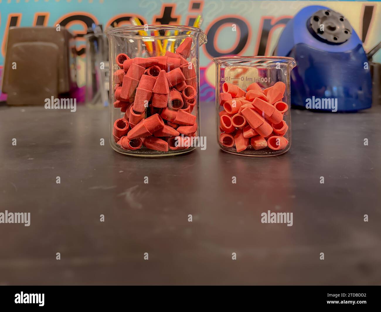 Pink pencil eraser caps in a clear glass laboratory beaker on a black
