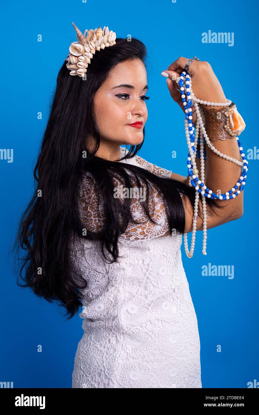 Beautiful, black-haired woman with shell tiara on her head holding and looking at pearl necklaces. Characterization of Iemanja. Stock Photo