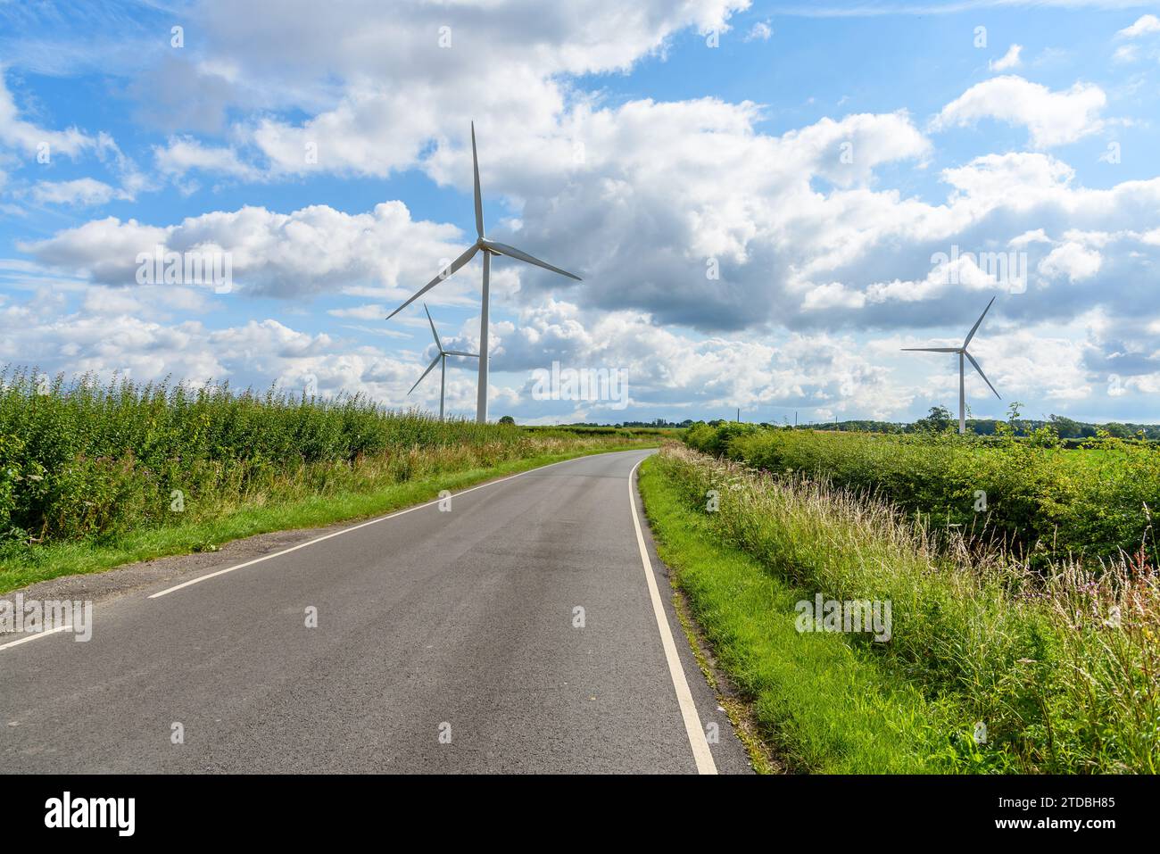 Deserted country road through a wind farm on a sunny summer day Stock Photo