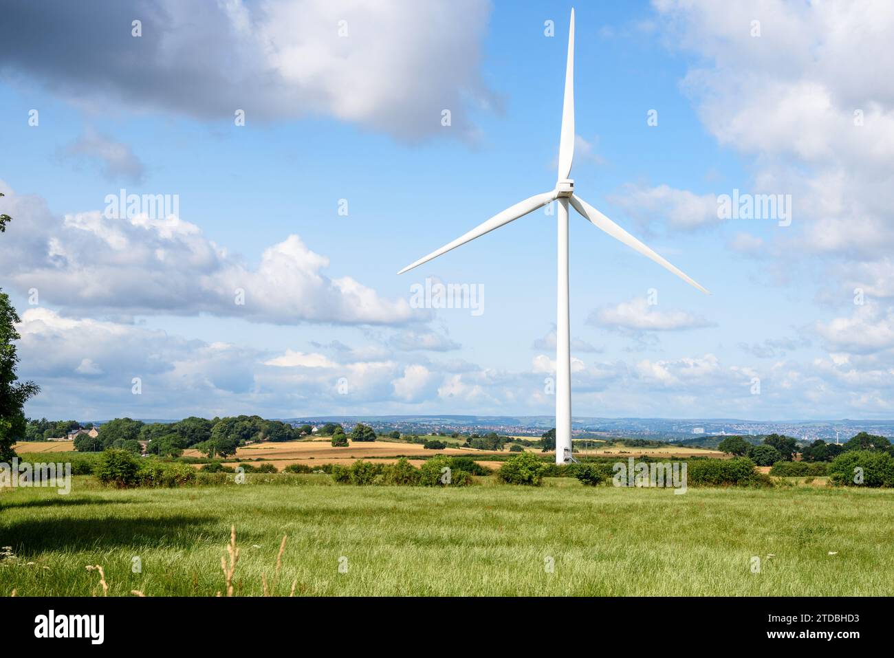 Tall wind turbine in a rolling rural landscape on a sunny summer day. A city is visible in background. Stock Photo