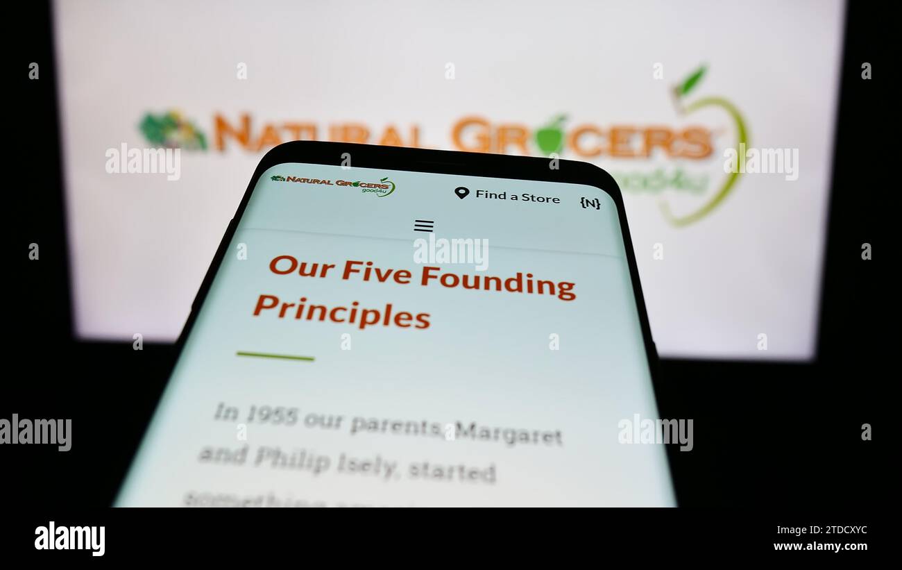 Mobile phone with website of retail company Natural Grocers by Vitamin Cottage Inc. in front of logo. Focus on top-left of phone display. Stock Photo