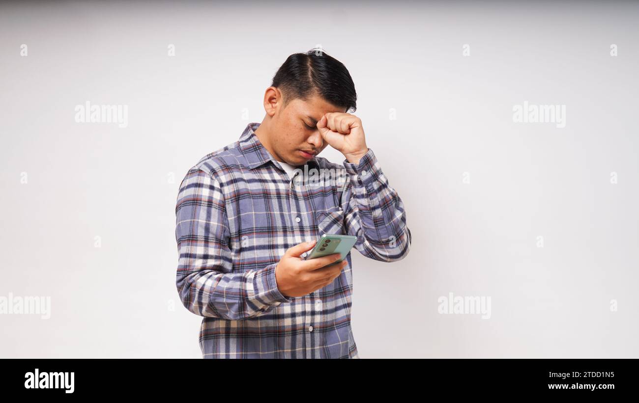 Young Asian man holding his mobile phone with sad and Confused expression on white background. studio shot Stock Photo
