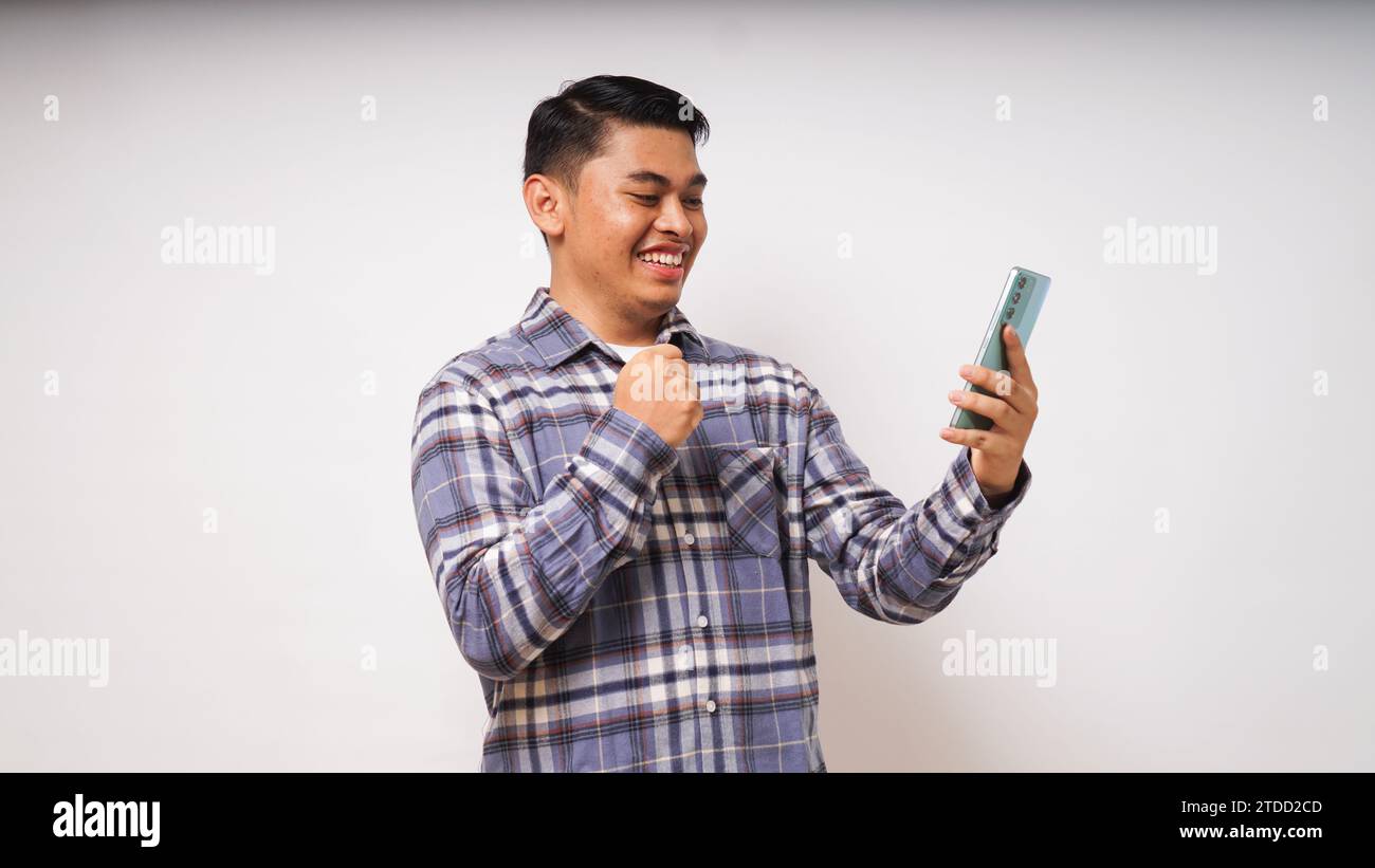 Young Asian man showing happy gesture while looking to his mobile phone on white background. studio shot Stock Photo