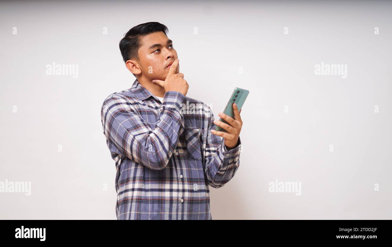 Young Asian man holding his mobile phone with sad and Confused expression on white background. studio shot Stock Photo