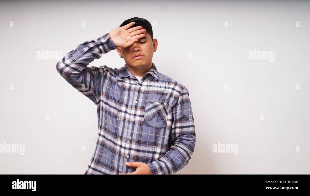 Unhappy sick young asian man suffer from terrible strong head pain, touching her forehead with closed eyes, studio shot, teenage boy have fever during Stock Photo