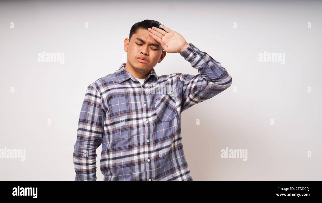 Unhappy sick young asian man suffer from terrible strong head pain, touching her forehead with closed eyes, studio shot, teenage boy have fever during Stock Photo