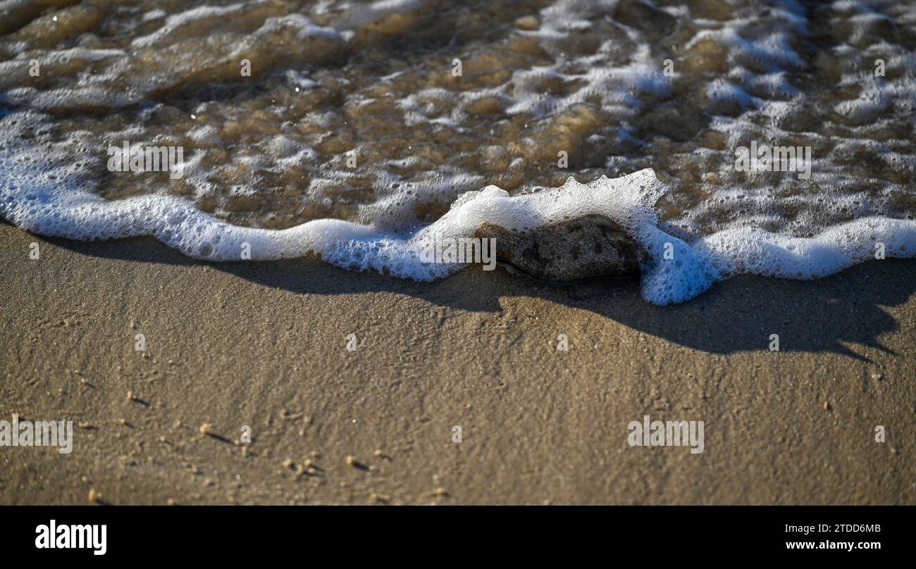 Close up high resolution image of a small wave covering a small rock on ...