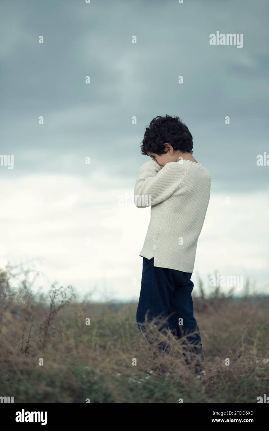 7 years old boy standing in the field head in hands crying Stock Photo