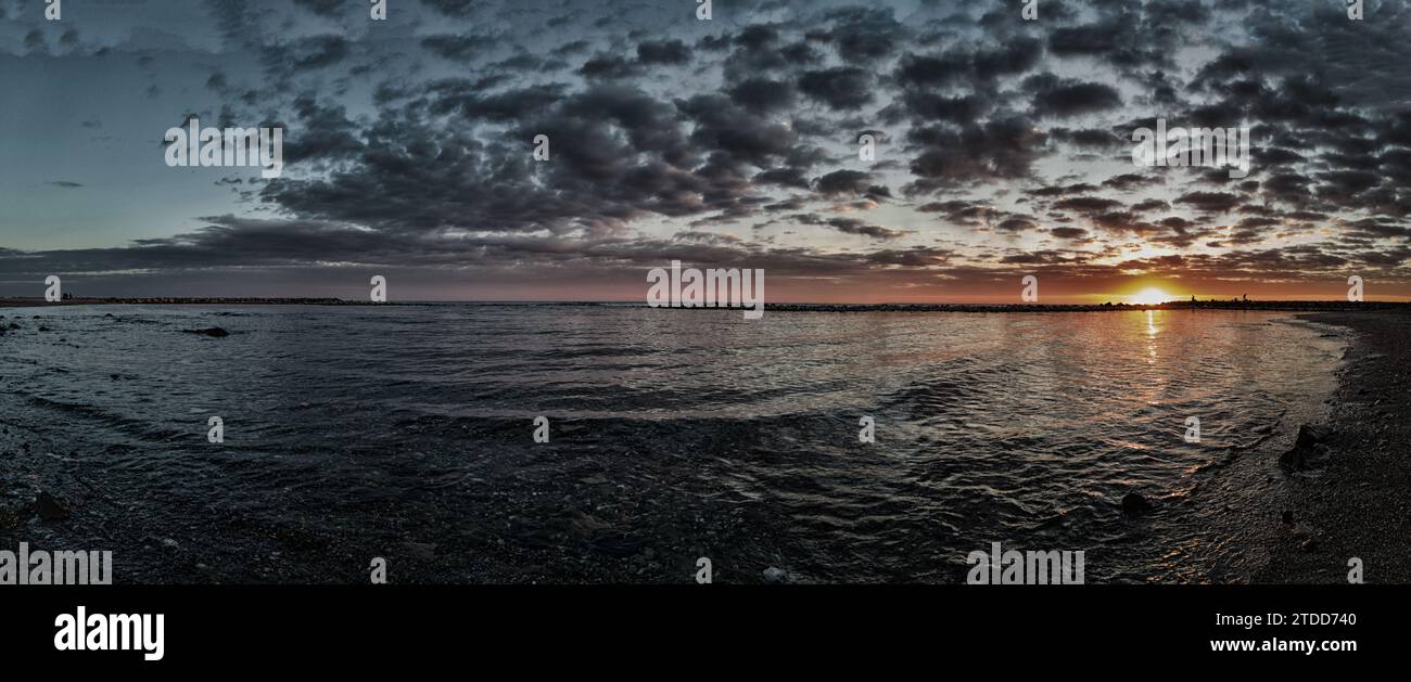Awesome panoramic 180 degrees of rough sea at sunset, a dramatic sky with amazing light and cloudscape of mammatus clouds between sunbeam reflections Stock Photo