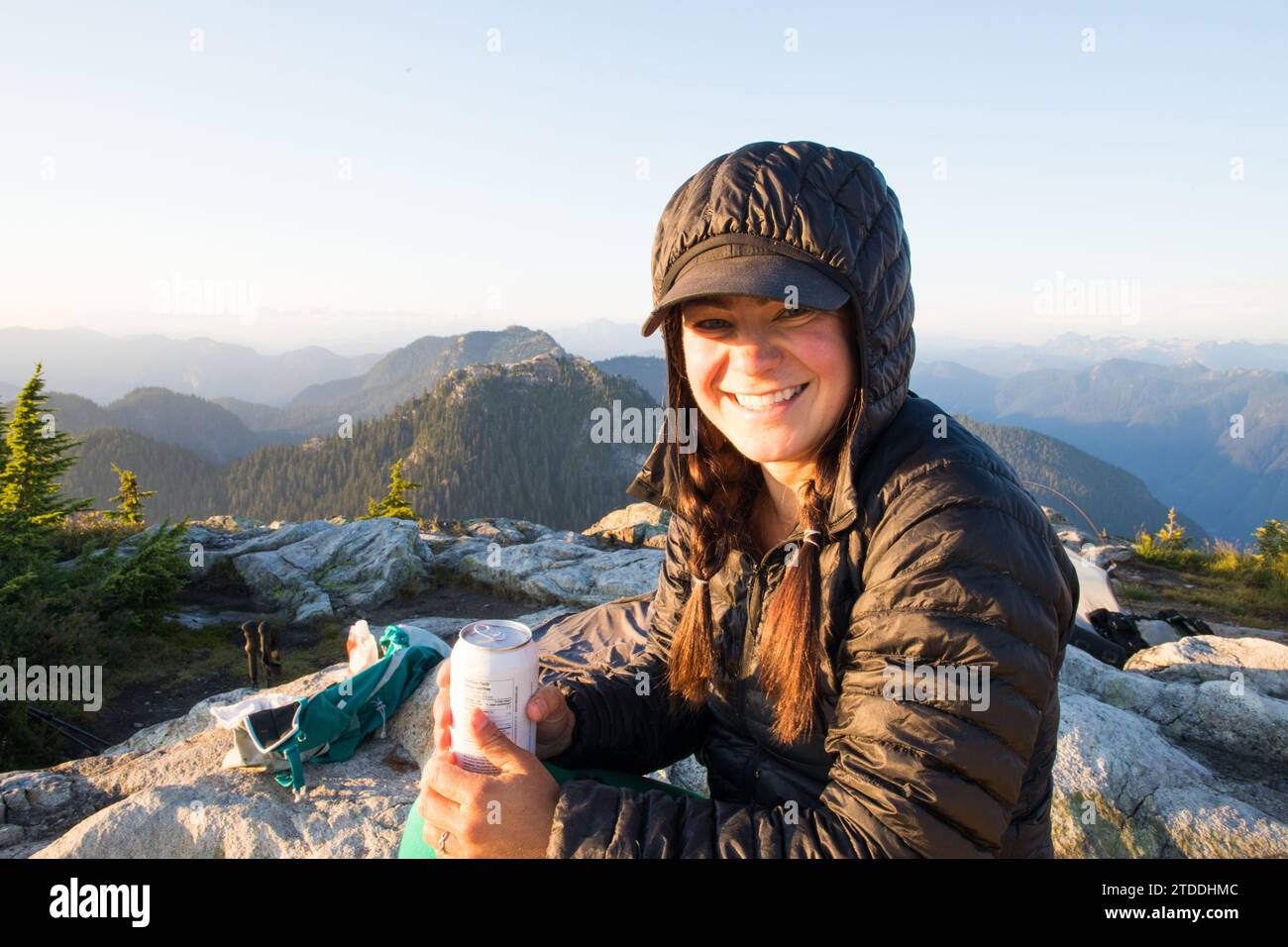 Fit woman smiling, holding drink on mountain summit Stock Photo