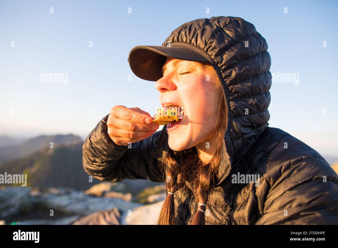 Active woman eats chips and salsa outdoors, on mountain. Stock Photo