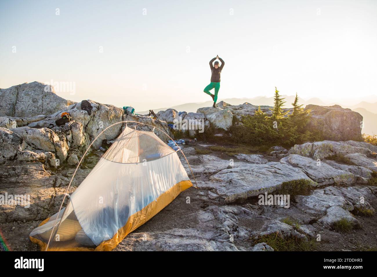 confident fit woman practices yoga (tree pose) on mountain summit. Stock Photo