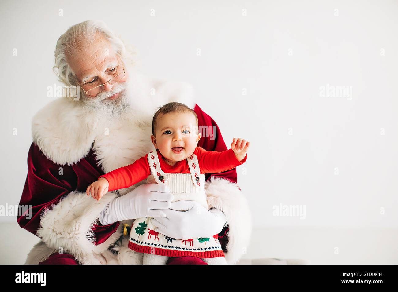 baby girl in christmas outfit sitting on santa's lap Stock Photo