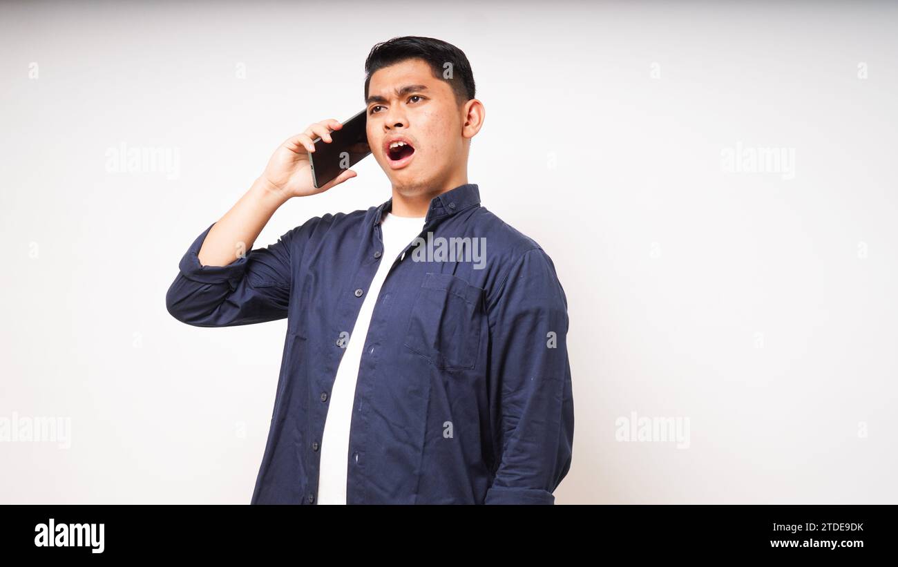 Asian young man using smartphone with shocked and surprised face expression. talk on smartphone. studio shot Stock Photo