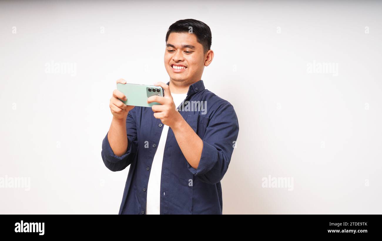 Excited young asian man playing game on smartphone on white background Stock Photo