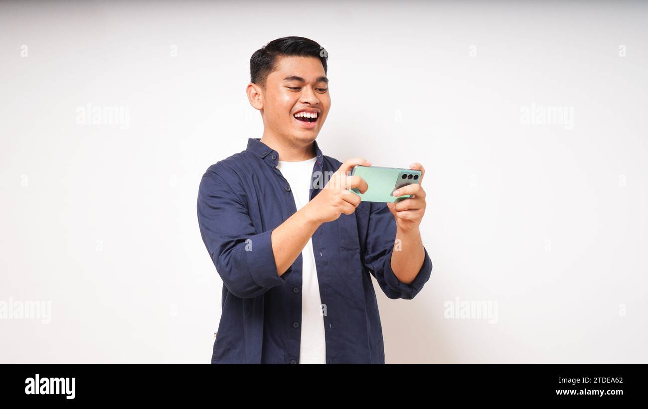 Excited young asian man playing game on smartphone on white background Stock Photo