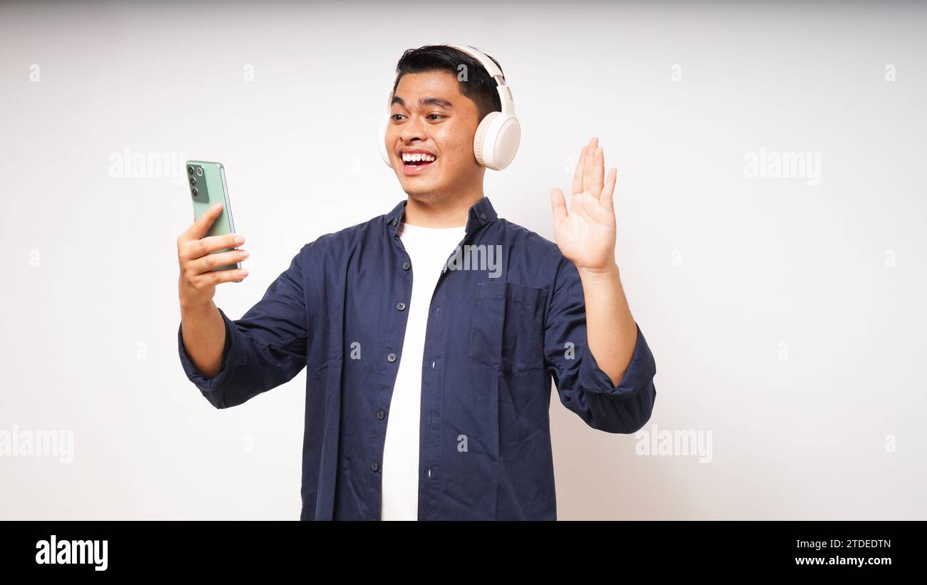 Happy young Asian man wearing wireless headphones listening to music from smartphone studio shot isolated on white background Stock Photo