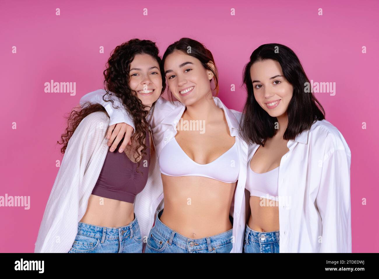 Four young women in casual attire posing against a pink background with confidence and style Stock Photo